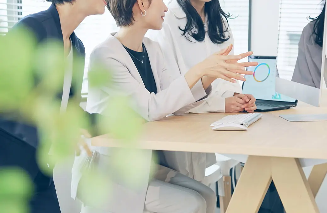 オフィスで白いジャケットを着た人物がテーブルで説明している様子。