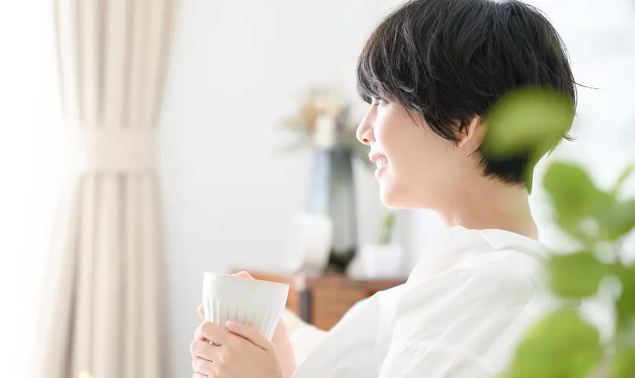 短髪の女性が白い服を着てカップを持ち微笑んでいる横顔の様子。